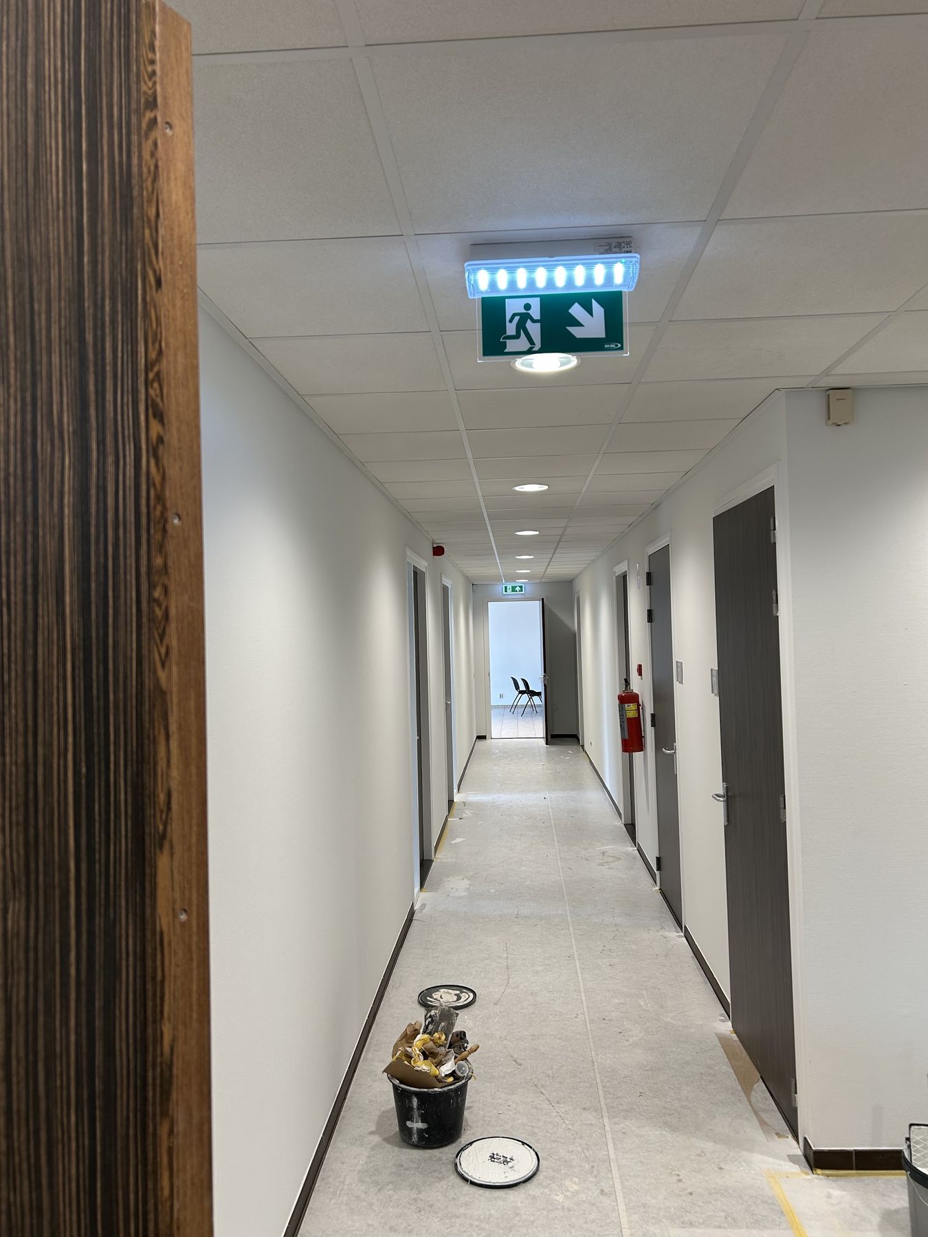 Gang in een bedrijfspand tijdens het schilderwerk, met witte wanden, grijze deuren en een afgedekte vloer