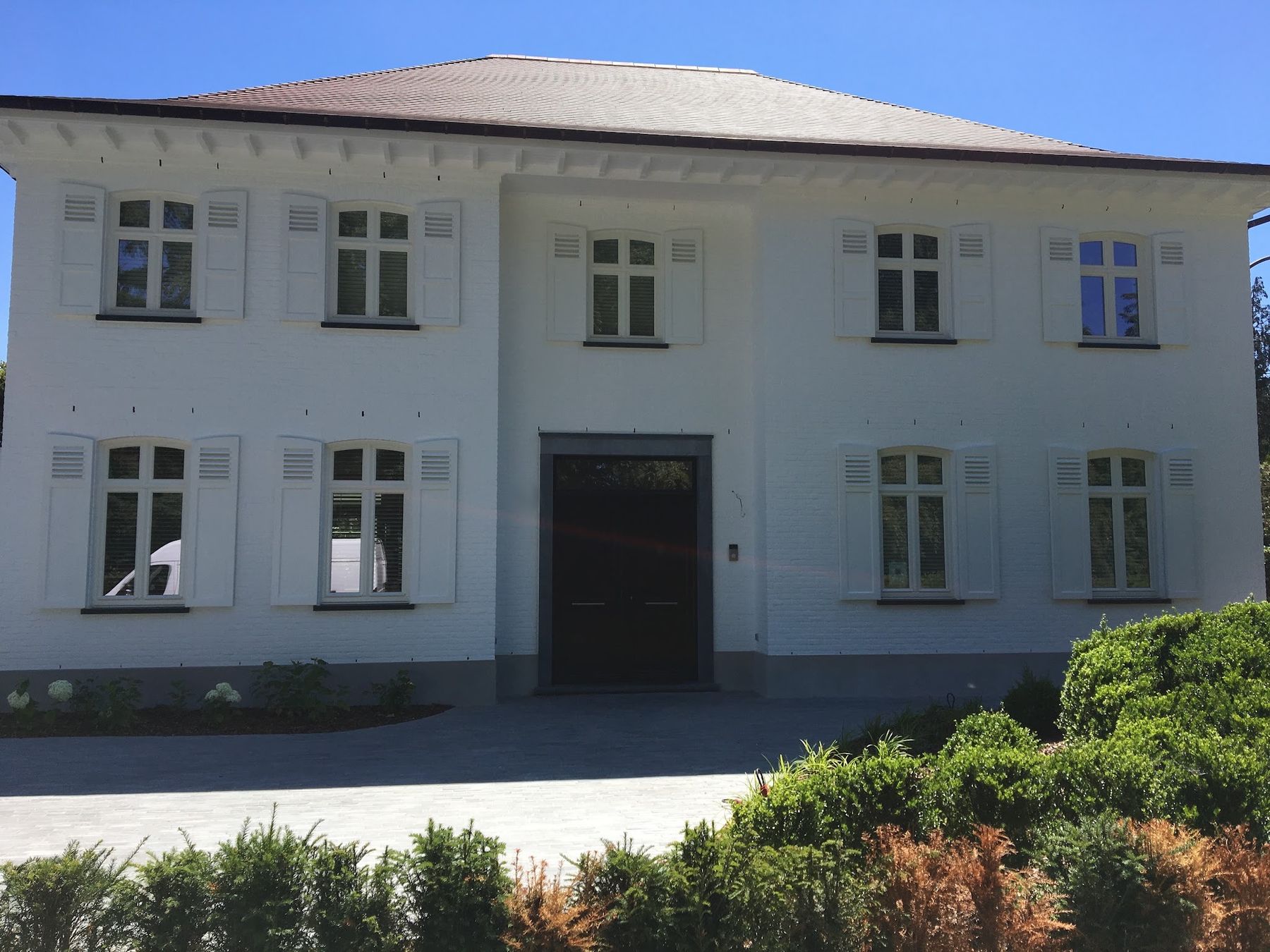 Grote witte villa met crèmekleurige luiken en een donkere dubbele voordeur, vers geschilderd