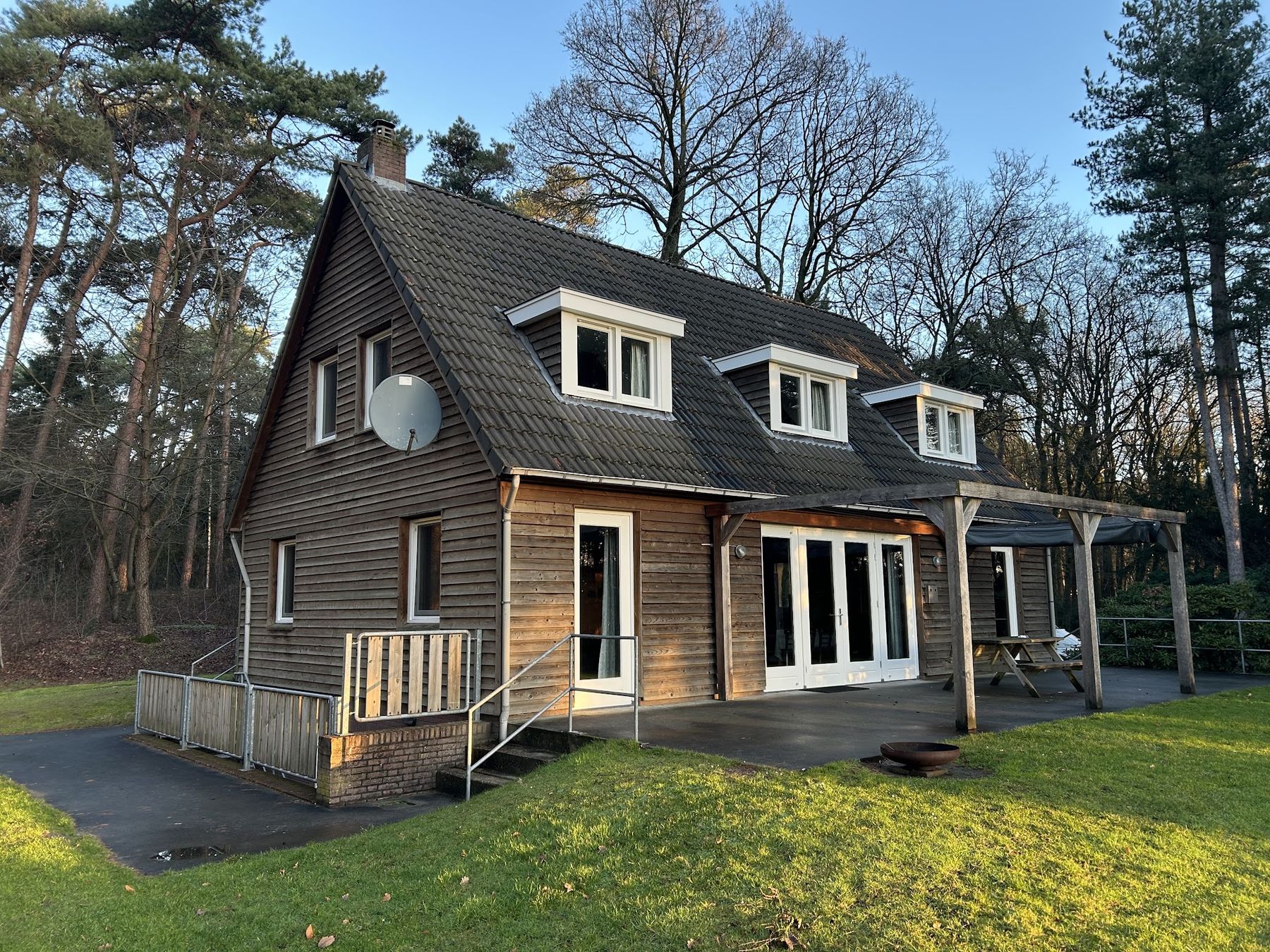 Houten woning tussen de dennen met vers geschilderde witte kozijnen, dakkapellen en tuindeuren in de lage winterzon