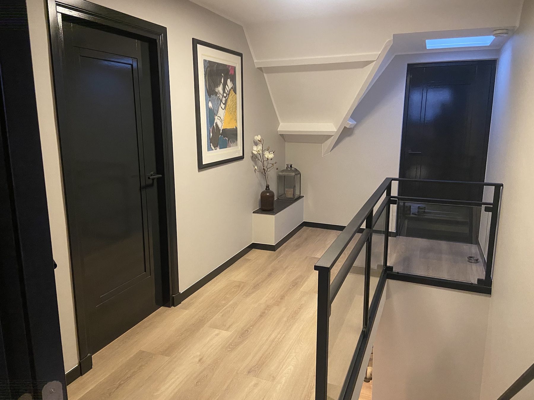 Overloop met zwarte hoogglans deuren en plinten, lichtgrijze wanden en een glazen balustrade