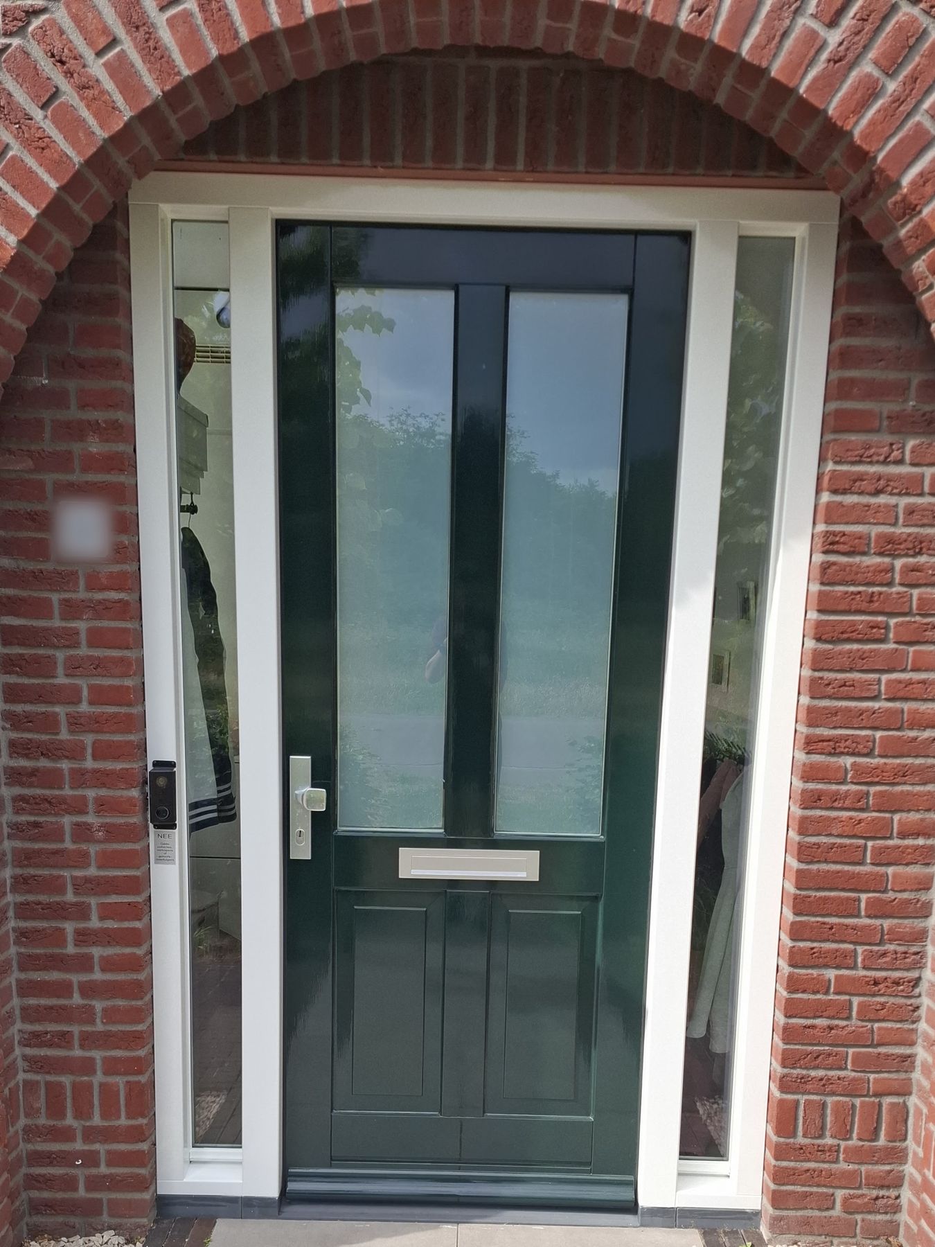 Donkergroene voordeur in hoogglans met crèmekleurige zijlichten onder een bakstenen boog